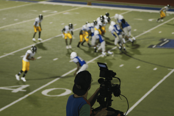Behind the scenes of cameraman filming wide shot of football play