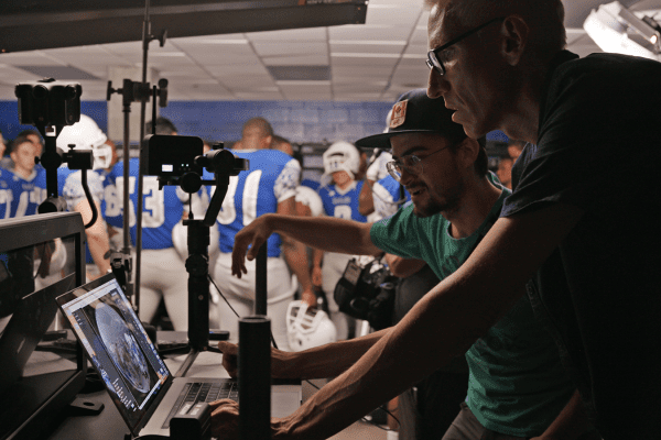 Behind the scenes photo of camera crew in football locker room filming scene