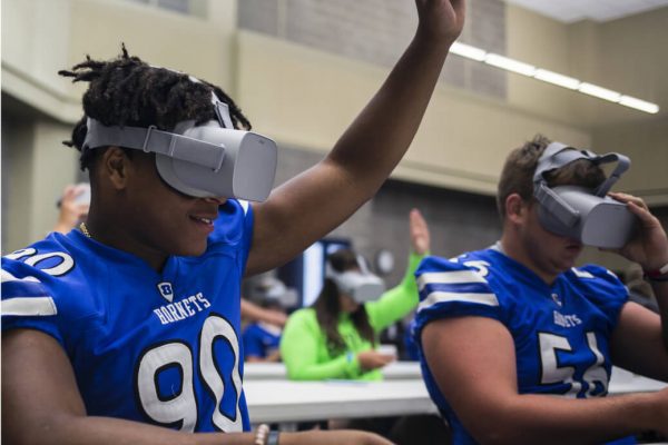 Students in football jerseys sitting at a desk wearing VR headsets